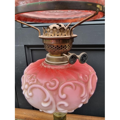 1423 - A Victorian brass and opaque glass oil lamp, with cranberry shade, 72.5cm high, (lacking chimne... 