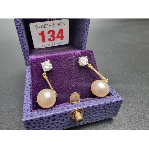 134 - A pair of 18ct white and yellow gold diamond and pearl pendant earrings, each set with a brilliant c... 