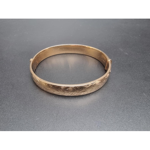 195 - A 9ct gold hinged bangle, having chased floral decoration to one side, Birmingham 1973, 19.1g.... 