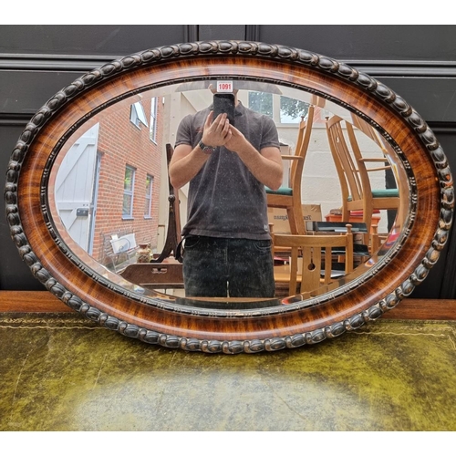 1091 - A 1920s mahogany and ebonized oval wall mirror, 62 x 87cm. 