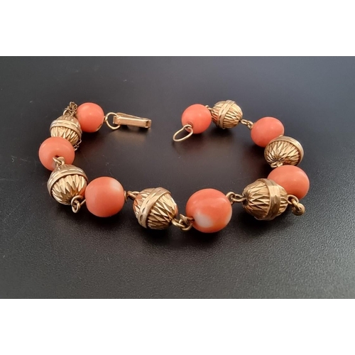 560 - A vintage yellow metal bracelet, set seven interspersed round coral beads, 21cm.