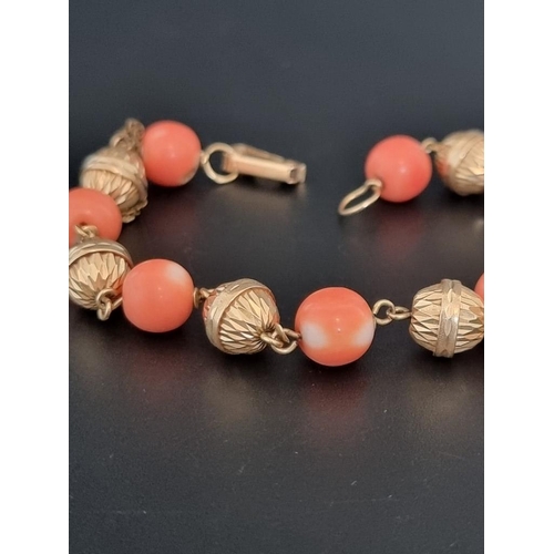 560 - A vintage yellow metal bracelet, set seven interspersed round coral beads, 21cm.