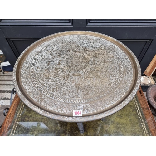 1061 - A brass circular table, on ebonized folding stand, 59cm diameter. 