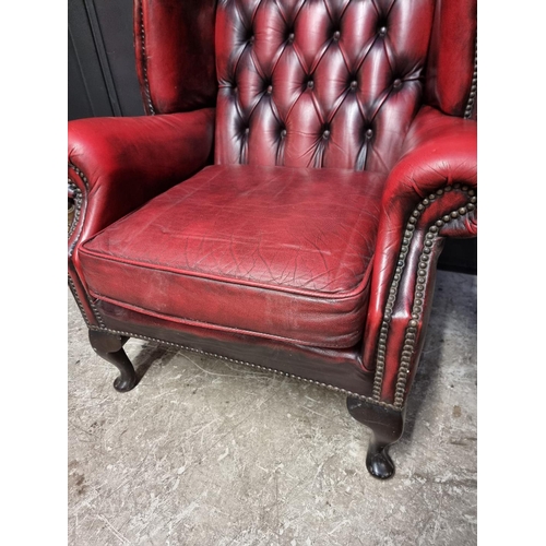 1077 - A reproduction button red leather wing armchair. 