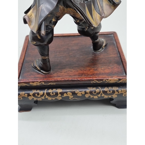 1228 - A Japanese bronze and parcel gilt figure of a Samurai, Meiji, signed Miyao, on hardwood stand, 23cm ... 