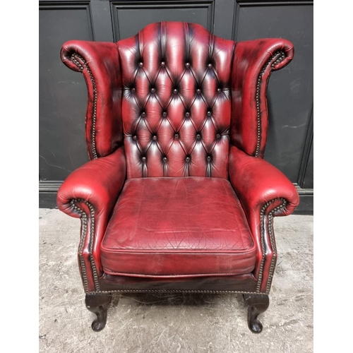 1077 - A reproduction button red leather wing armchair. 