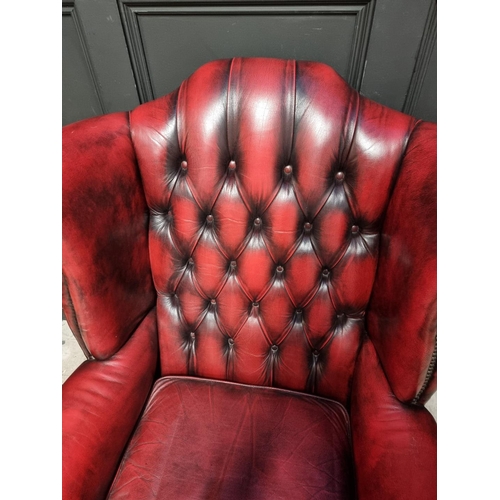 1077 - A reproduction button red leather wing armchair. 