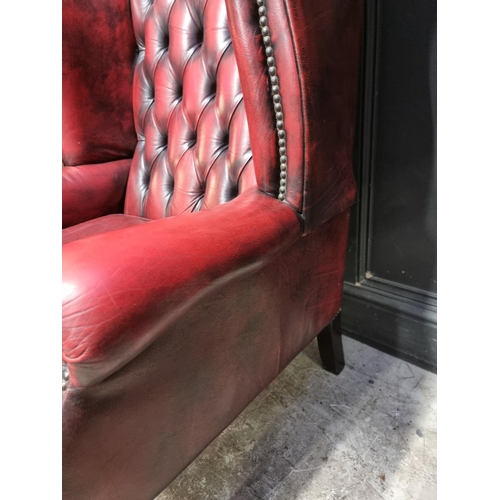 1077 - A reproduction button red leather wing armchair. 