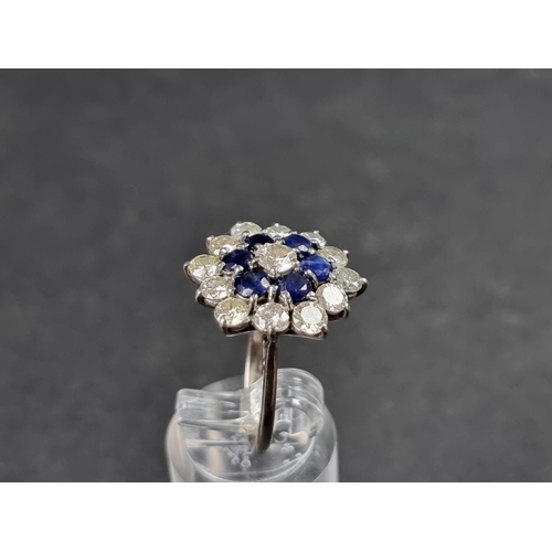 937 - A diamond and sapphire floral cluster ring, set central brilliant cut diamond surrounded by a row of... 