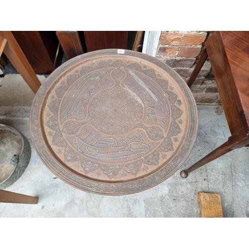 1021 - A Cairo ware brass table top and folding stand, with Islamic script, 65cm diameter. ... 