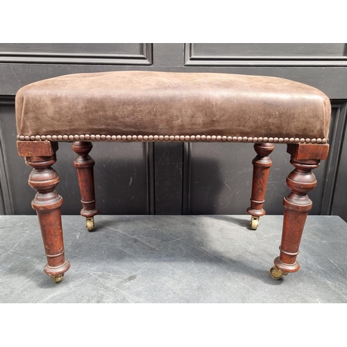 1089 - A mahogany and buttoned leather stool, on brass casters, 60.5cm wide.