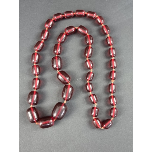 321 - A cherry amber style necklace, 72cm long, having forty barrel shaped beads, the largest 26mm, gross ... 