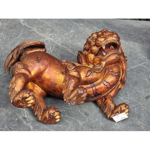 1523 - A Chinese carved giltwood lion dog, 23.5cm long; together with another Chinese carved giltwood figur... 