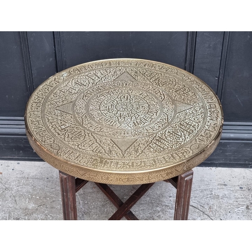 1042 - A brass top folding occasional table, inscribed with Islamic script, 59.5cm diameter.... 