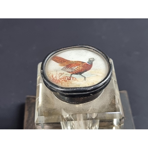 114 - A silver lidded glass inkwell on silver mounted stand, the lid inset with painted pheasant, by ... 