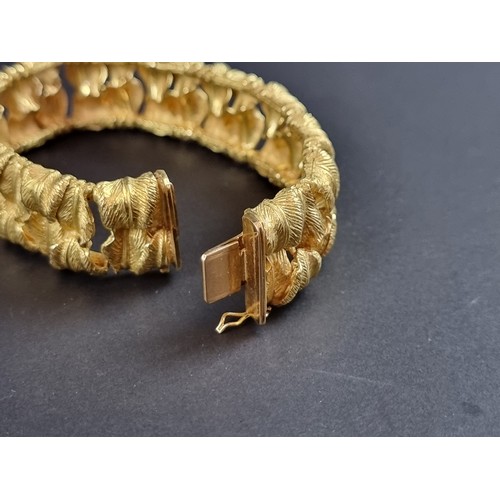 238 - A chunky yellow metal bracelet, designed as two rows of stylised leaves, stamped 'T 18k/0750 078', 1... 