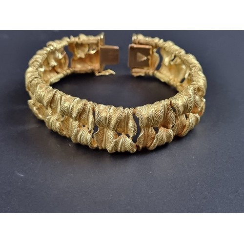 238 - A chunky yellow metal bracelet, designed as two rows of stylised leaves, stamped 'T 18k/0750 078', 1... 