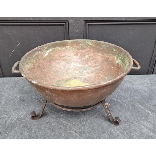 1521 - A large copper twin handled vessel, 62cm wide, on steel tripod stand.