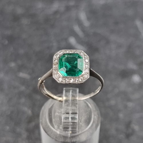 329 - An emerald and diamond cluster ring, the central trap cut emerald of approximately 1.4ct, surrounded... 