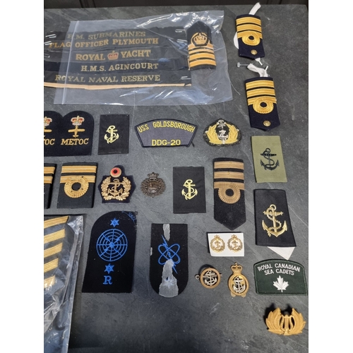 27 - A group of Royal Navy insignia and hat tallies, including royal yacht, HMS Agincourt and HM Submarin... 