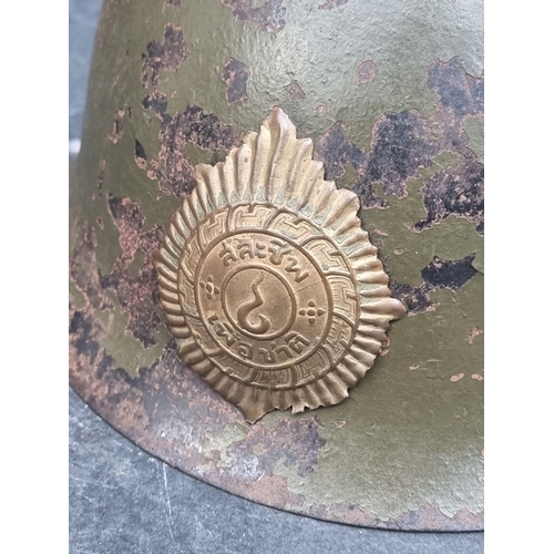 61 - A Korean War Thai infantry steel helmet, with lining, chinstrap and badge, purposed from a WWII Japa... 