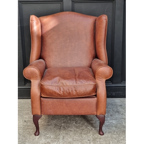 1068 - A Laura Ashley tan leather wing armchair, with integral footrest.