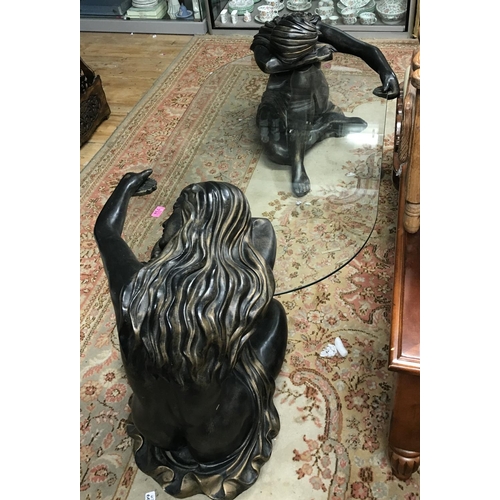 758 - LARGE GLASS COFFEE TABLE SUPPORTED BY 2 RESIN RISQUE LADIES AT EITHER END - 170CMS X 80CMS OVERALL -... 