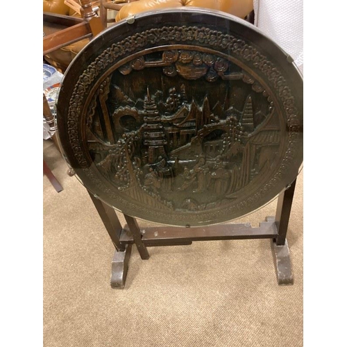 148 - A Japanese hardwood occasional table, the circular tilt top with carved figures and pagodas in a lan... 