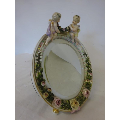 93 - An old German porcelain dressing mirror decorated with cherubs, one ball foot missing.