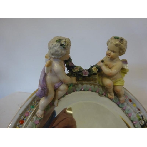 93 - An old German porcelain dressing mirror decorated with cherubs, one ball foot missing.