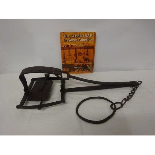 245 - A rare antique hand forged metal trap together with a book, The Steel Trap in North America. (2)