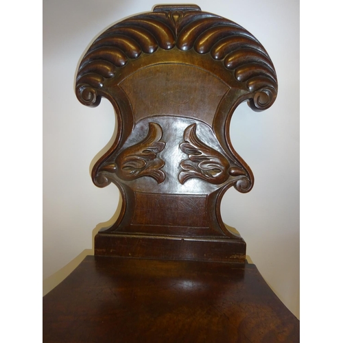 125 - A pair of early 19th century mahogany hall chairs having shaped and carved backs.