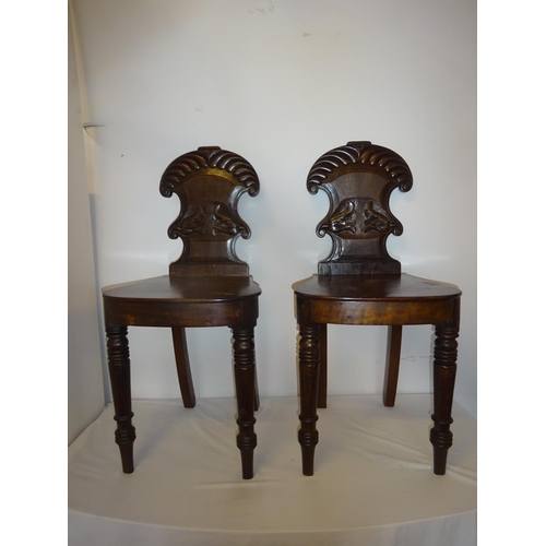 125 - A pair of early 19th century mahogany hall chairs having shaped and carved backs.