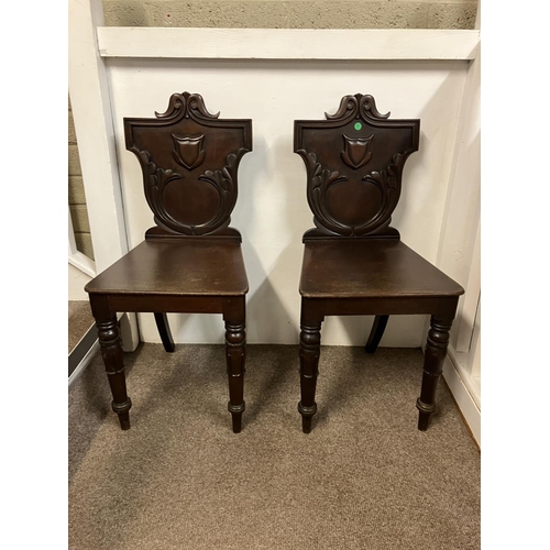 102 - A pair of antique mahogany hall chairs having shaped backs with carved decoration and raised on tuli... 