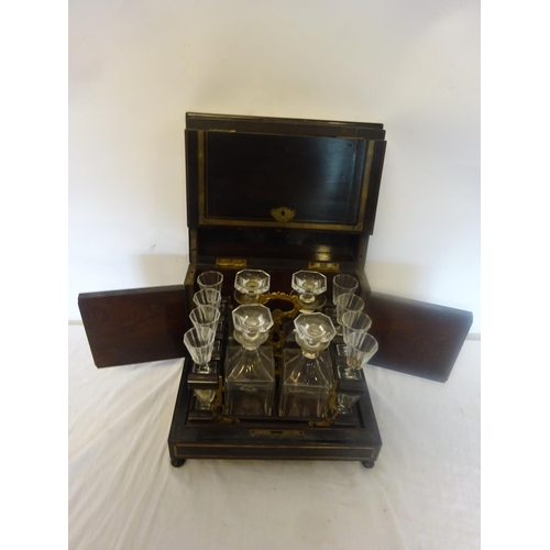 84 - Antique brass inlaid decanter box fitted with four decanters and fourteen small glasses (2 missing).