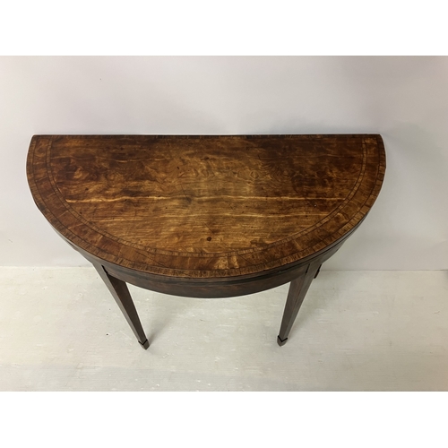 109 - A Georgian nicely figured mahogany demi lune card table, the fold over top with rosewood cross bandi... 