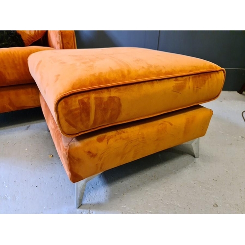 99 - A designer armchair and matching footstool, with two cushions, upholstered in orange velvet.