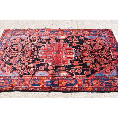 434 - A Middle Eastern red ground wool rug, hand woven in deep pile, the centre depicting stylized figures... 