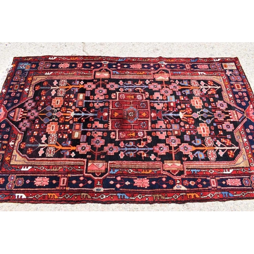 435 - A Middle Eastern red ground wool rug, the centre depicting stylized figures and architecture amidst ... 