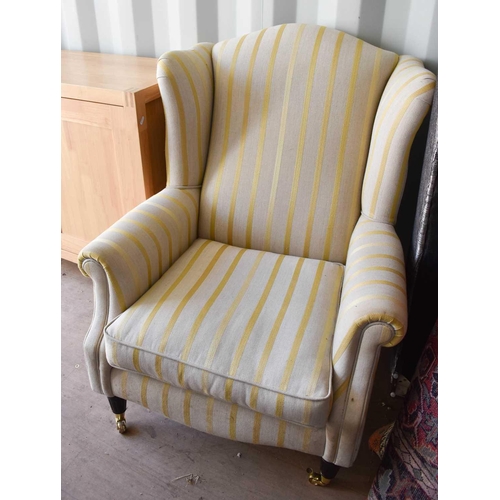 487 - A modern wingback armchair upholstered in cream with gold bands.