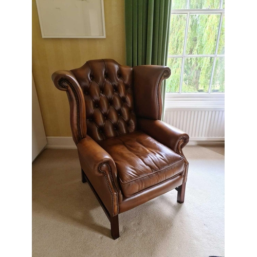 529 - A 20th century wing back armchair, with button back leather upholstery, seat cushion, on block legs ... 