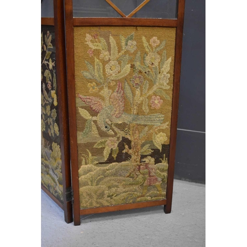 562 - An early 20th century mahogany and glass fire screen set with two needlework panels depicting birds ... 