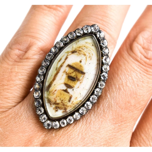 25 - A Victorian white metal and paste mourning ring of marquise form, the enamel centre depicting an urn... 