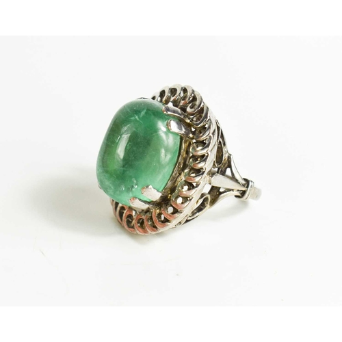 3 - An impressive 18ct white gold and boulder emerald ring, the stone bordered by decorative swirl borde... 