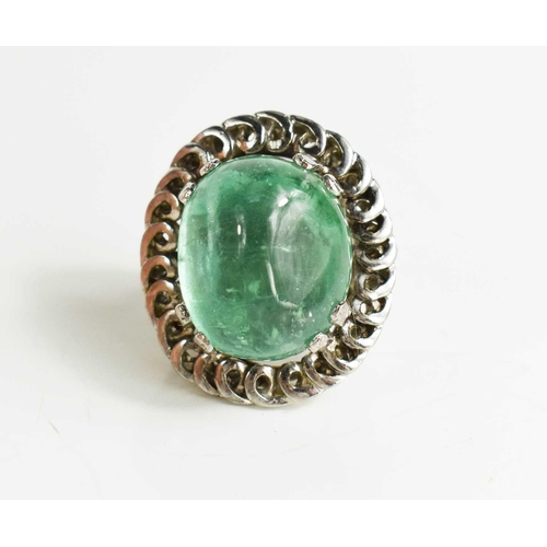 3 - An impressive 18ct white gold and boulder emerald ring, the stone bordered by decorative swirl borde... 