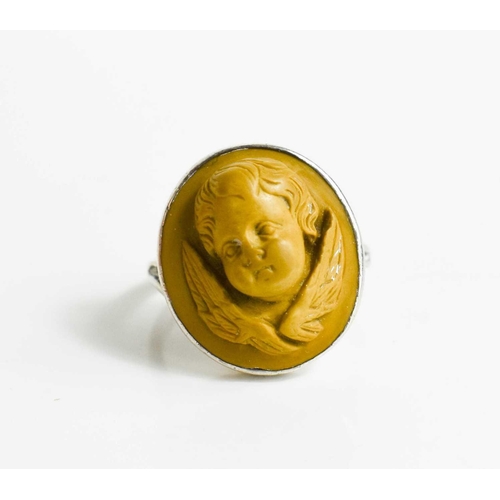 37 - A white metal ring, with relief moulded stone ring in the form of a winged cherub head, size N/O, 6g... 