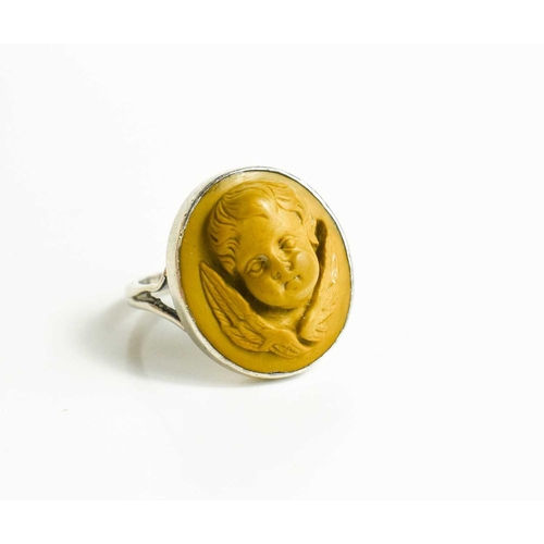 37 - A white metal ring, with relief moulded stone ring in the form of a winged cherub head, size N/O, 6g... 