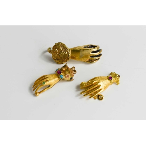 54 - Two gold hand form clasps, set with gemstones together with a gilt metal example, the gold testing t... 