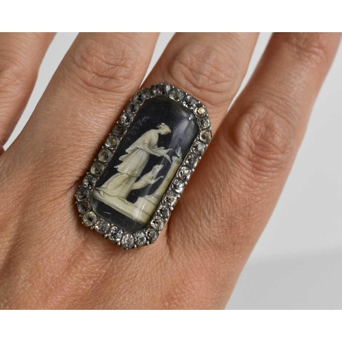 59 - A Victorian white metal and paste mourning ring with an enamelled centre depicting a woman beside do... 