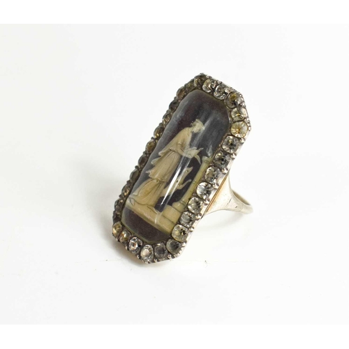 59 - A Victorian white metal and paste mourning ring with an enamelled centre depicting a woman beside do... 